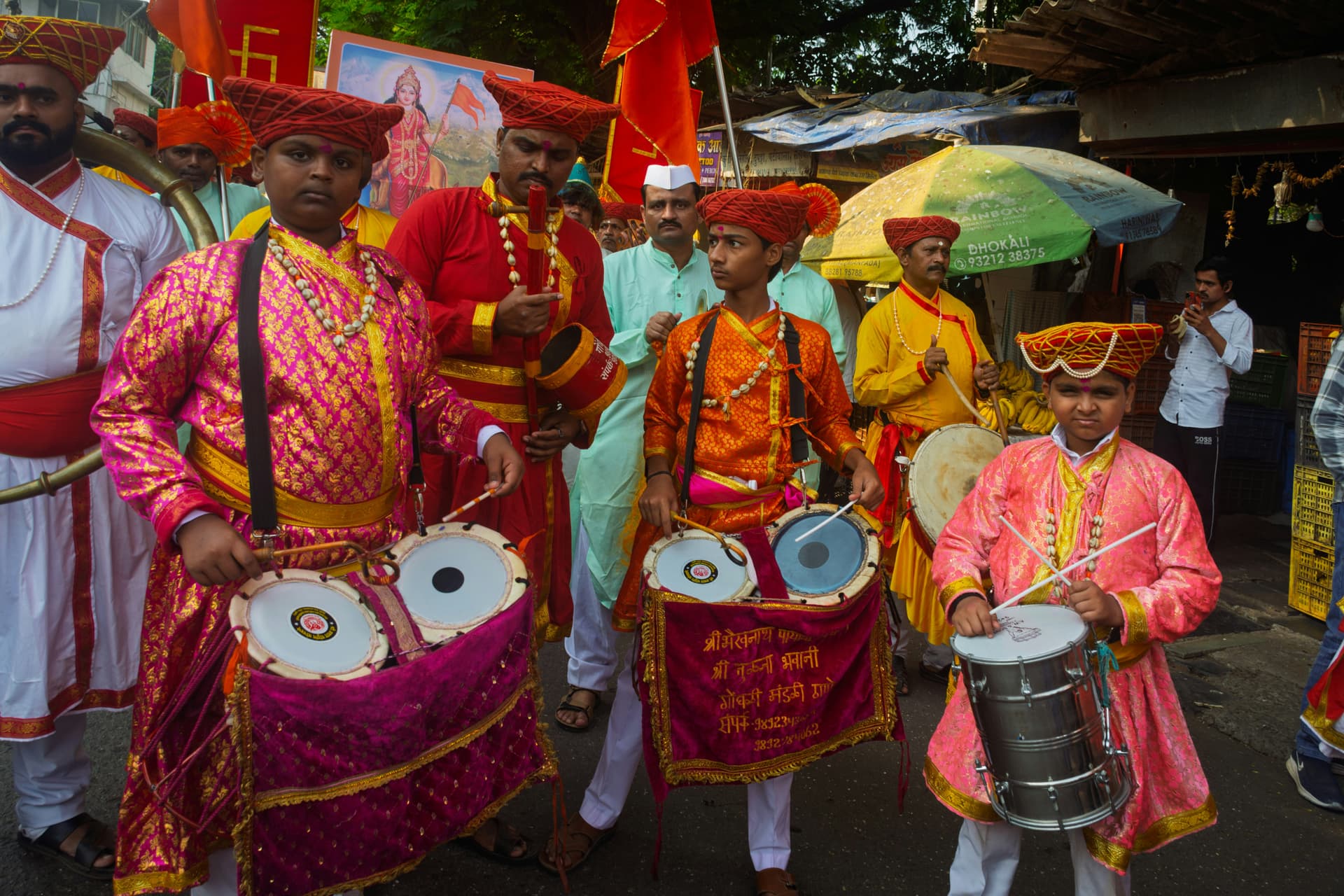 Men in colorful traditional attire play drums during a procession.